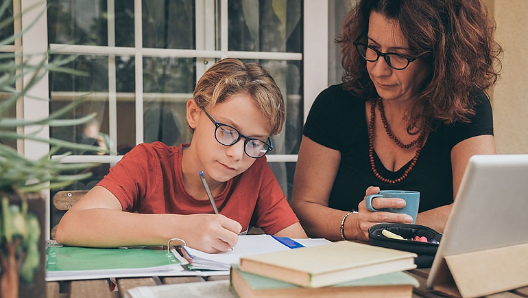 Fachkraft der Familienpflege hilft Kind beim Erledigen der Hausaufgaben.