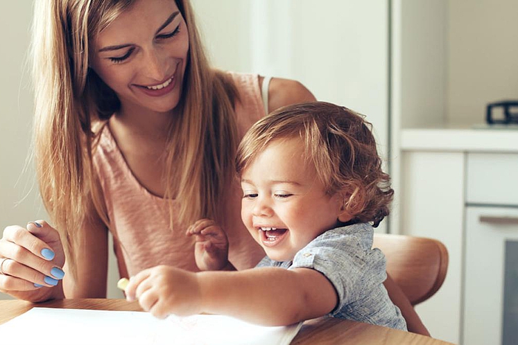 Fröhliche Tagesmutter und lustiges Kind beim Spielen im Wohnzimmer